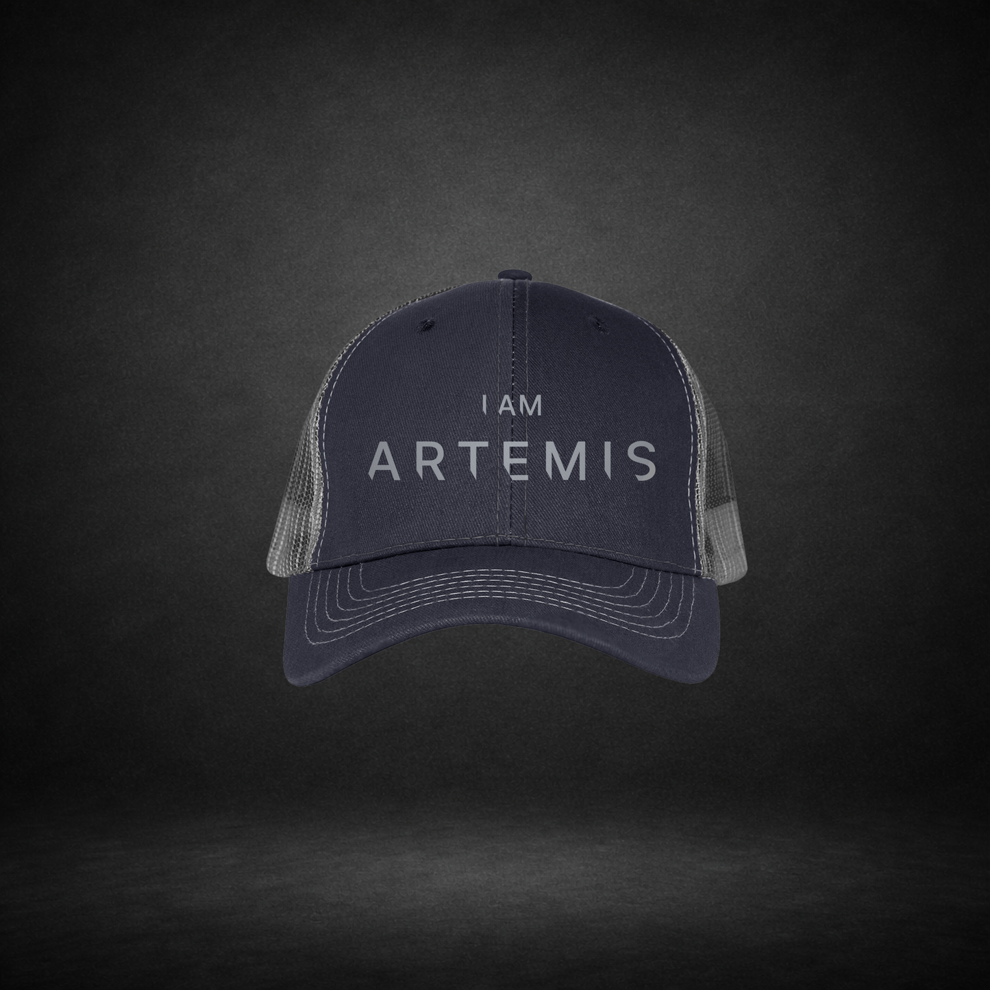 Navy blue cap with 'I AM ARTEMIS' text on a dark gray background